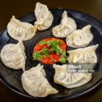 Veg steamed momo. Nepalese Traditional dish Momo stuffed with vegetables and then cooked and served with sauce on a ceramic black plate, selective focus on the subject